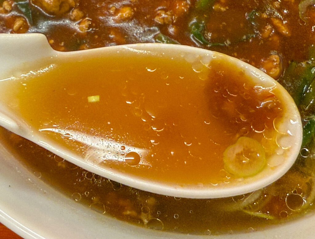 スープをすくったレンゲが印象的なスタミナラーメン。醤油スープと餡の二層構造が美しい。