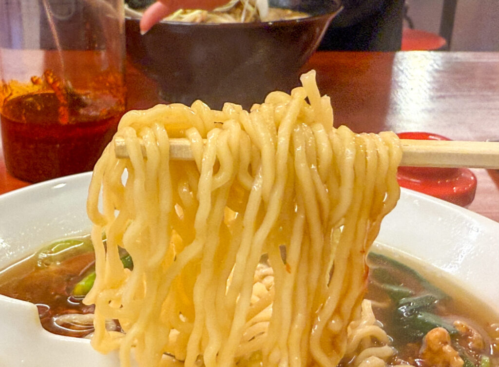 箸で持ち上げたスタミナラーメンの麺。あんがしっかり絡み、食欲をそそるカット。