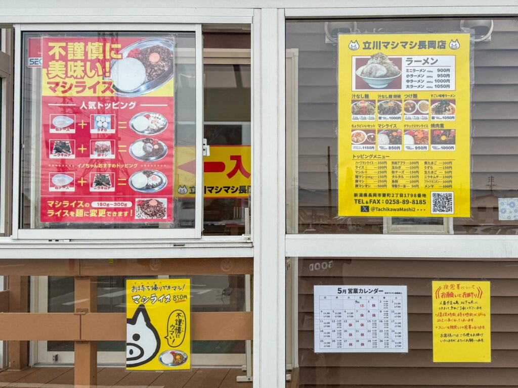 立川マシマシ長岡店の窓に貼られた営業案内とおすすめメニュー。店内外の情報が充実