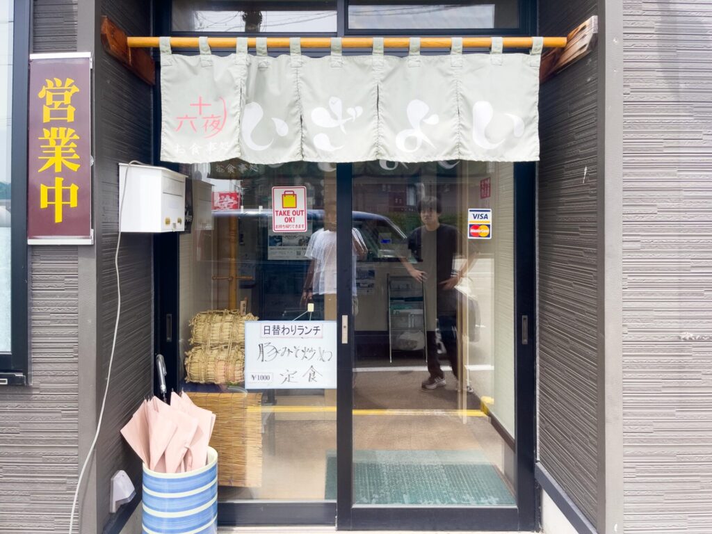 『いざよい』の暖簾がかかった正面入口と、日替わりランチの案内