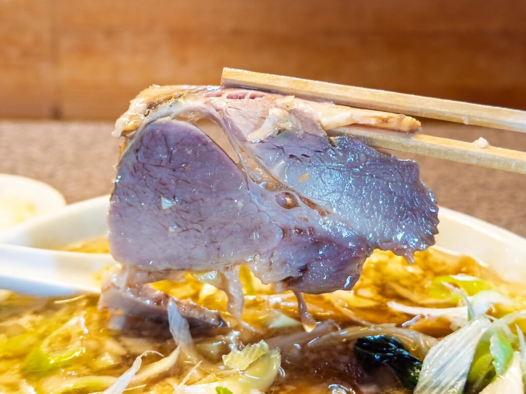 肉厚でしっとりとしたチャーシューを箸で持ち上げたシーン