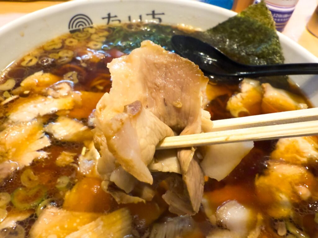 チャーシューメンのチャーシューを箸で持ち上げた様子。厚みと柔らかさが伝わる
