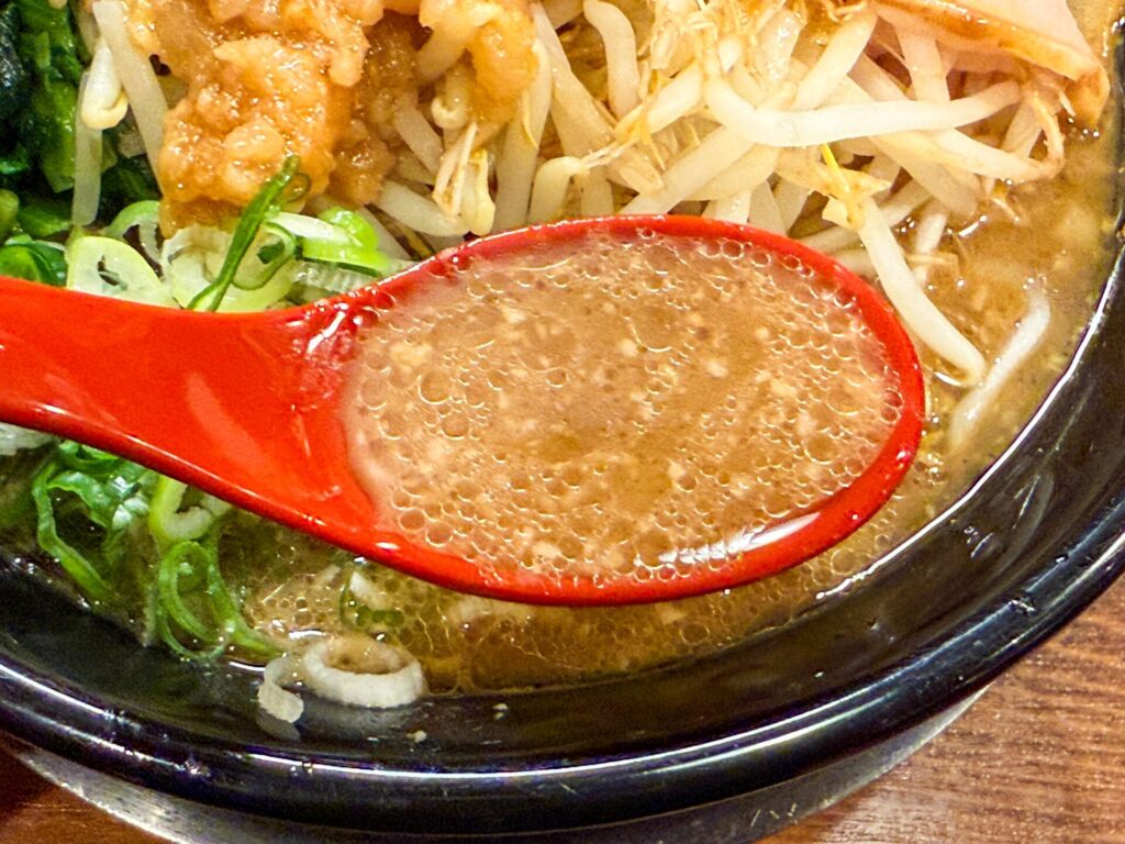 レンゲにすくった濃厚豚骨スープ。背脂が浮かび、コク深い味わいが伝わる。