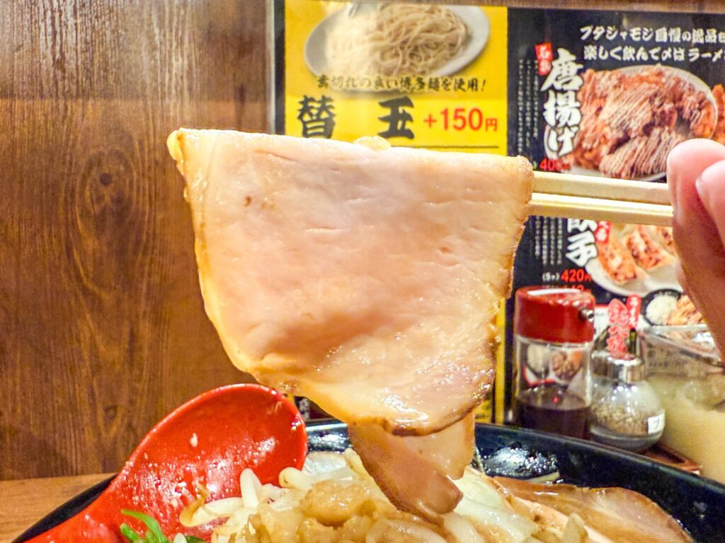 大きめサイズのチャーシューを箸で持ち上げた様子。柔らかく肉の旨味が楽しめる。